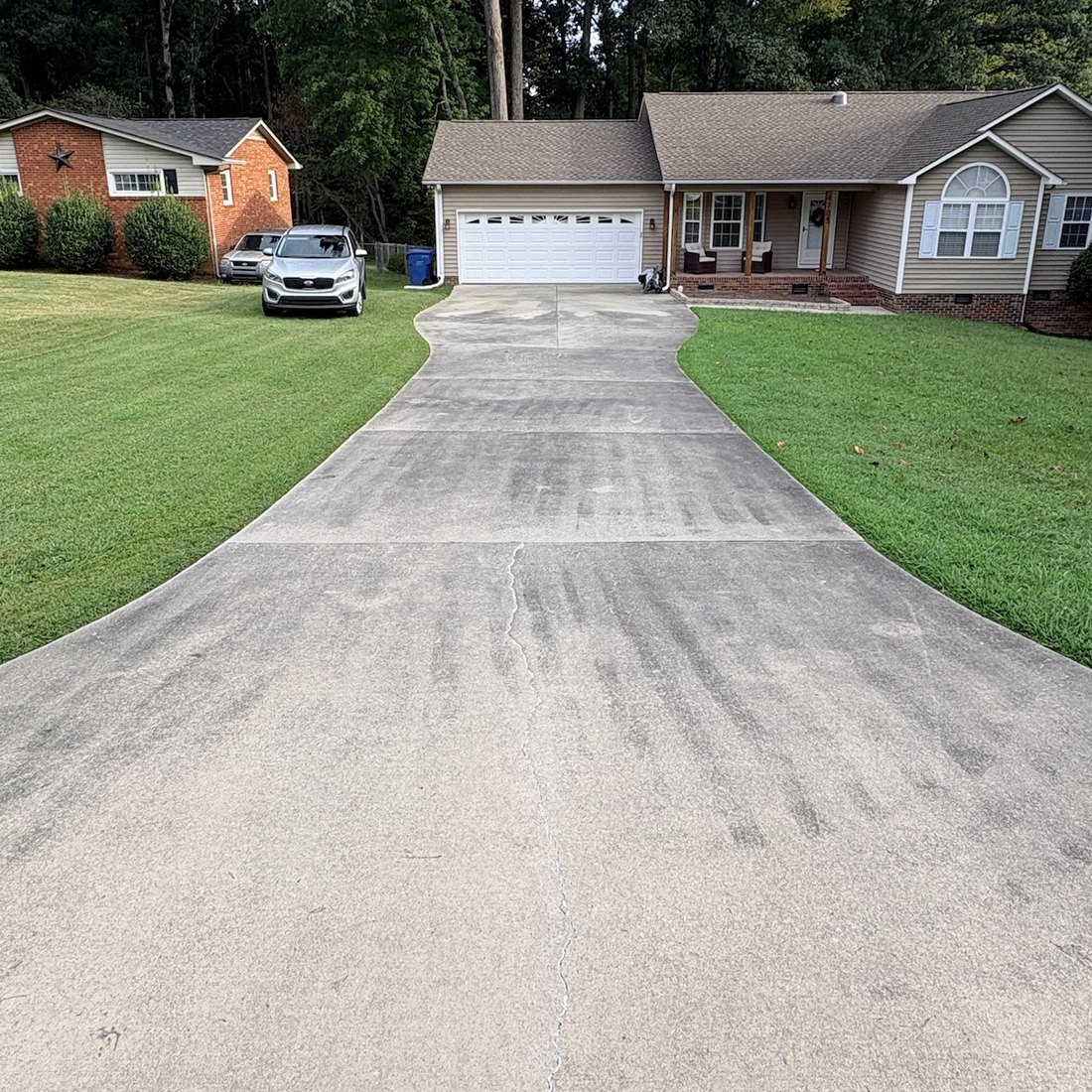 The same concrete driveway before pressure washing, streaked with dark grey dirt and tire marks