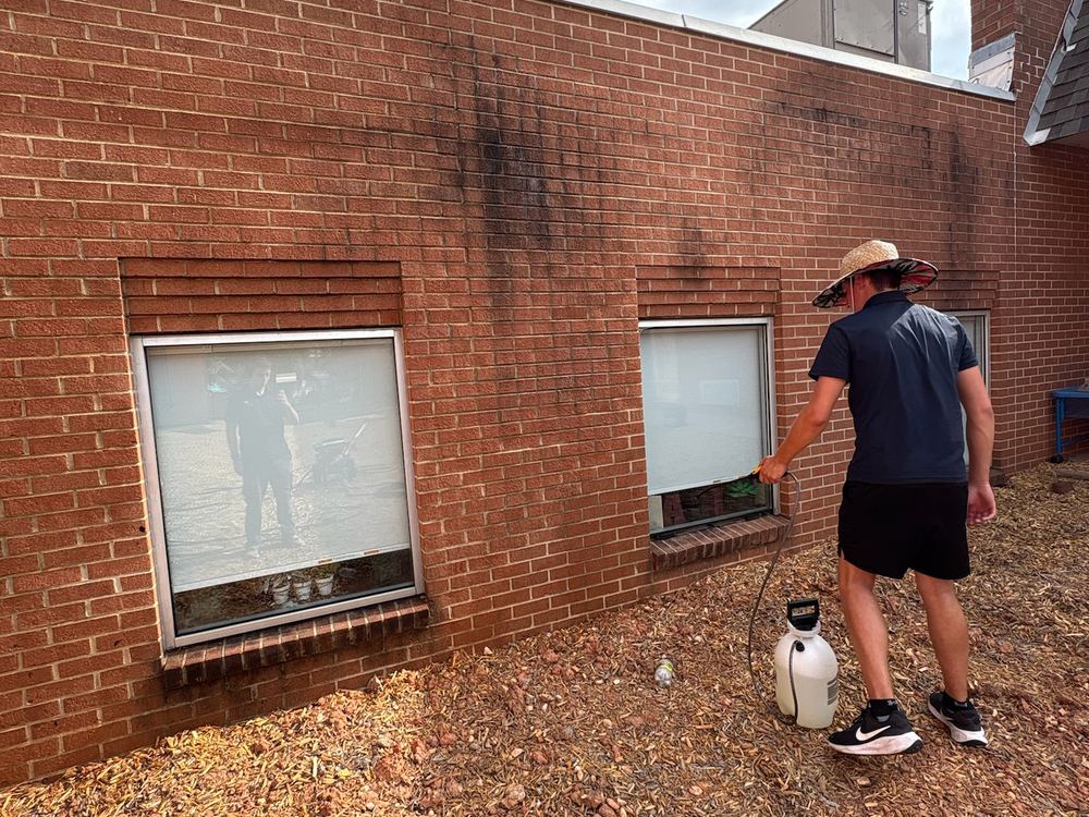 A Ninja Cleaning technician applying cleaning solution to a stained commercial brick wall